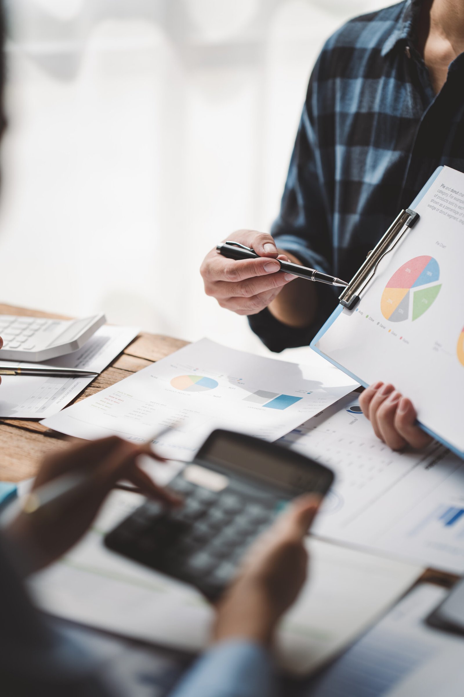 Colegas jóvenes debaten sobre gráficos de precios empresariales y analíticos utilizando calculadoras y ordenadores portátiles para calcular